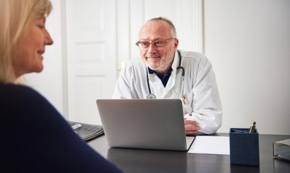 Smiling adult doctor listening patient at laptop